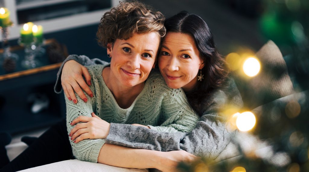 Kaksi ystävystä halaa toisiaan kauniissa ja tunnellmallisessa kuvassa ja katsovat suoraan kameraan.